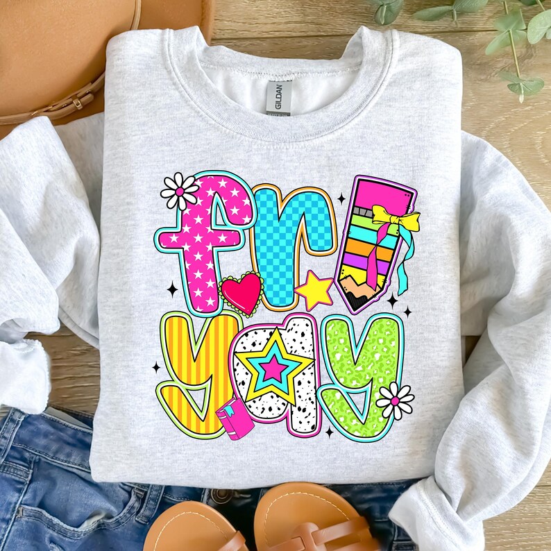 May include: A gray sweatshirt with a colorful graphic that says "Fri-yay" with a pencil, stars, and hearts.