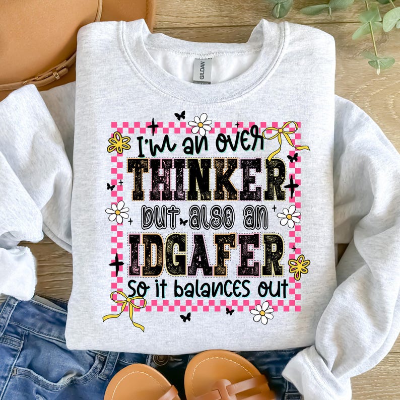 May include: Light gray sweatshirt with the text "I'm an over thinker but also an IDGAF-er so it balances out." The text is in black, pink, and white, with floral and butterfly accents. The sweatshirt is a casual style.