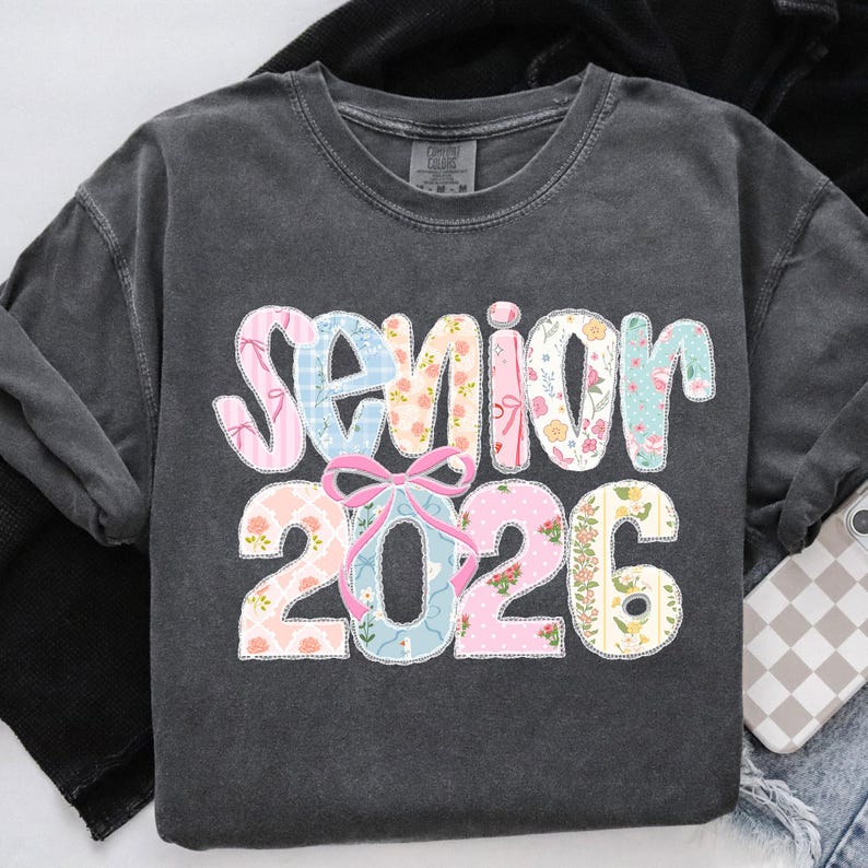 Puede incluir: Sudadera gris oscuro con la palabra "Senior" y el a&ntilde;o "2026" en un dise&ntilde;o floral y estampado colorido. La palabra "Senior" est&aacute; en patrones florales rosas, azules y blancos. El a&ntilde;o "2026" est&aacute; en patrones florales rosas y amarillos.