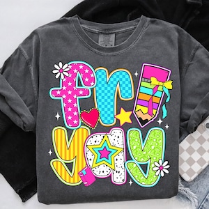 May include: A gray t-shirt with a colorful graphic that says "fri-yay" with a pencil, a star, a heart, and flowers.
