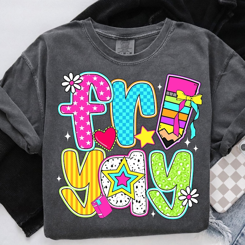 May include: A gray t-shirt with a colorful graphic that says "fri-yay" with a pencil, a star, a heart, and flowers.