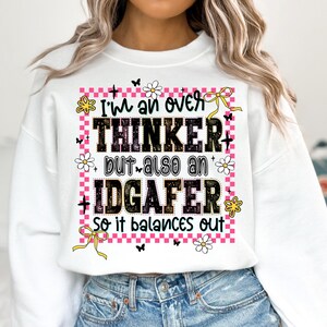 May include: White sweatshirt with the text "I'm an over THINKER but also an IDGAFER so it balances out." The text is in black, with a pink checkered border, flowers, butterflies, and yellow bows.