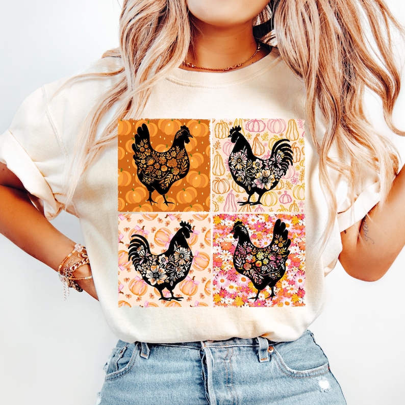 May include: Cream-colored t-shirt featuring a four-panel design with black chicken silhouettes. Each panel has a different background: pumpkins, flowers, and a mix of both. The chickens are filled with floral patterns.