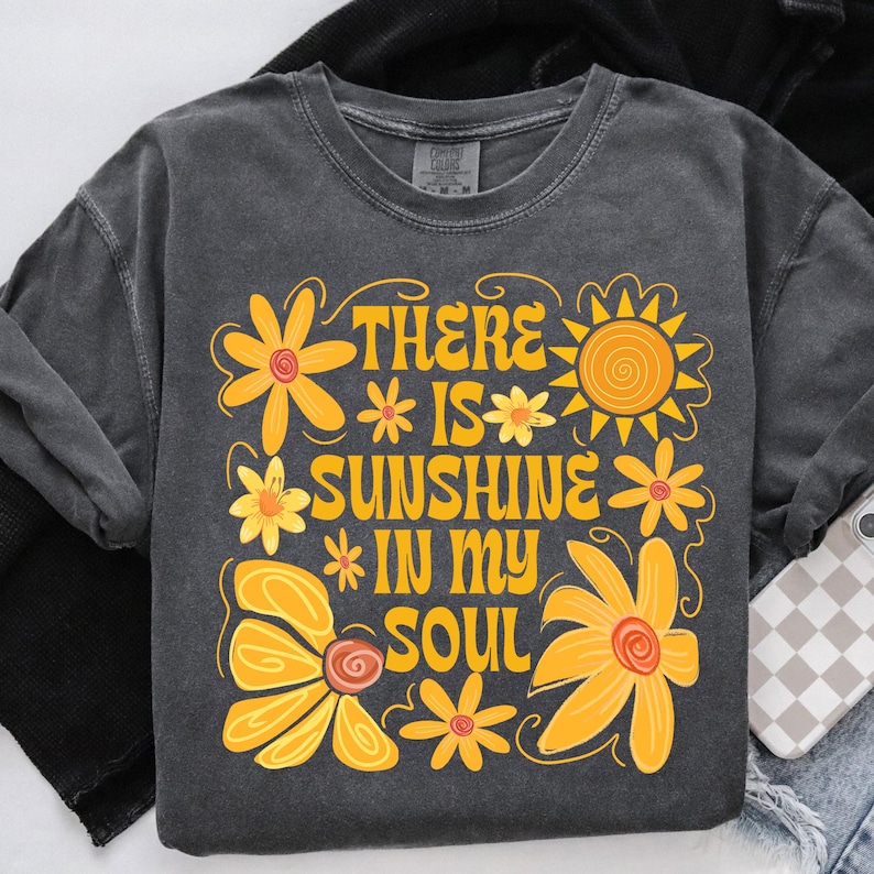 May include: A dark gray t-shirt with a yellow and orange floral design and the text "There is sunshine in my soul".