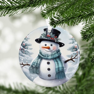 May include: A round Christmas ornament featuring a snowman with a black top hat, green scarf, and a carrot nose. The snowman is standing in a snowy winter scene with pine trees.
