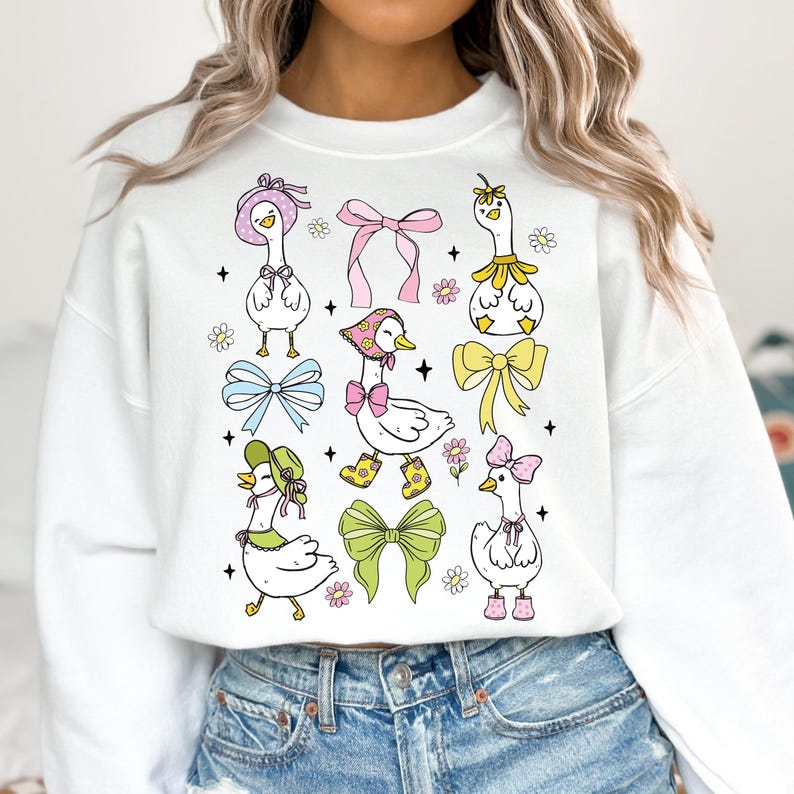 Puede incluir: Sudadera blanca con un estampado gr&aacute;fico colorido de gansos con sombreros y lazos. Los gansos est&aacute;n rodeados de flores y estrellas.