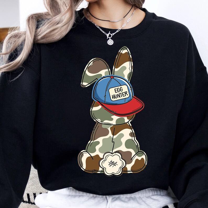 May include: Black sweatshirt with a cartoon bunny wearing a blue and red baseball cap that says "Egg Hunter". The bunny is camouflage patterned.