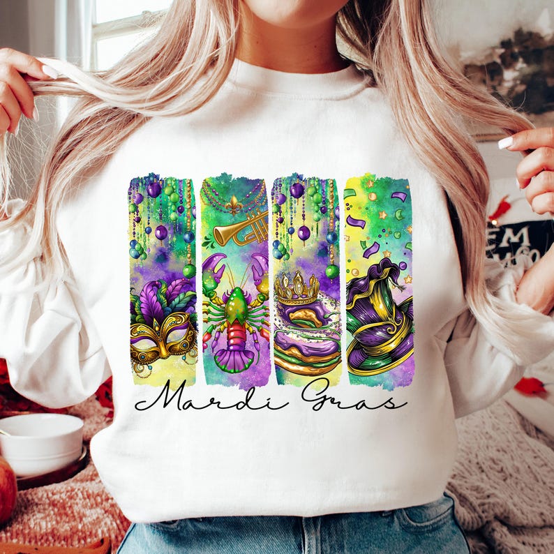 May include: White sweatshirt with a colorful Mardi Gras design featuring a mask, a crawfish, a king cake, and a jester's hat. The text "Mardi Gras" is printed below the design.