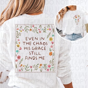 May include: White sweatshirt featuring a floral cross design and the text "Even in the chaos his grace still finds me" framed by flowers and leaves. The design incorporates various colorful flowers.