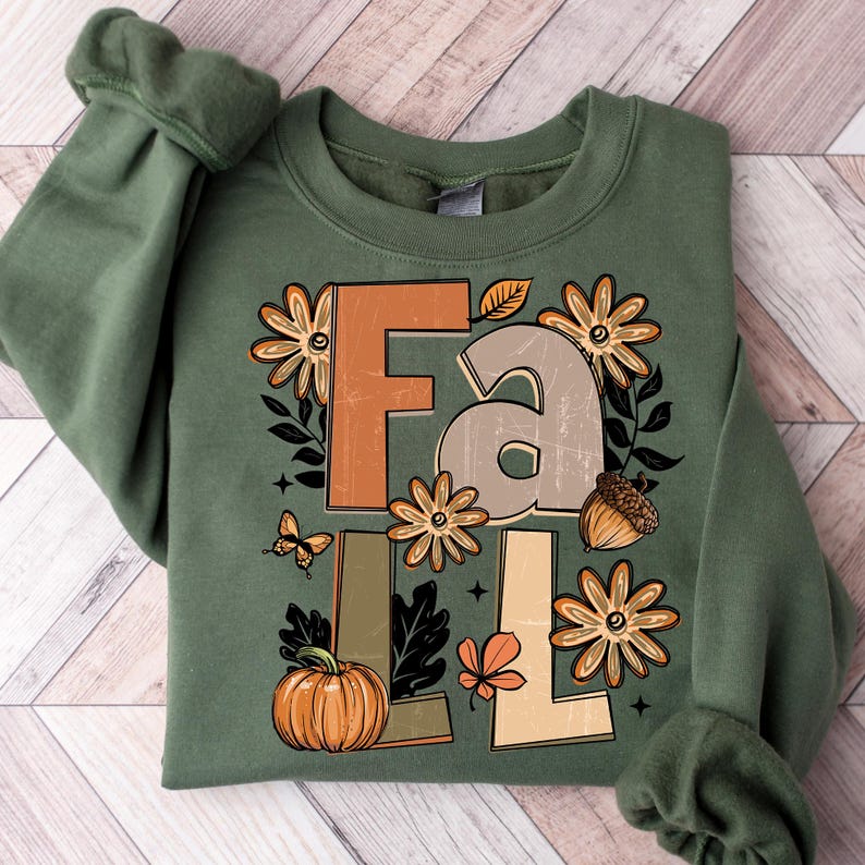 May include: Green sweatshirt with the word "FALL" in large, decorative letters. The design includes fall-themed graphics like flowers, a pumpkin, an acorn, a butterfly, and leaves. The sweatshirt is a crew neck style.