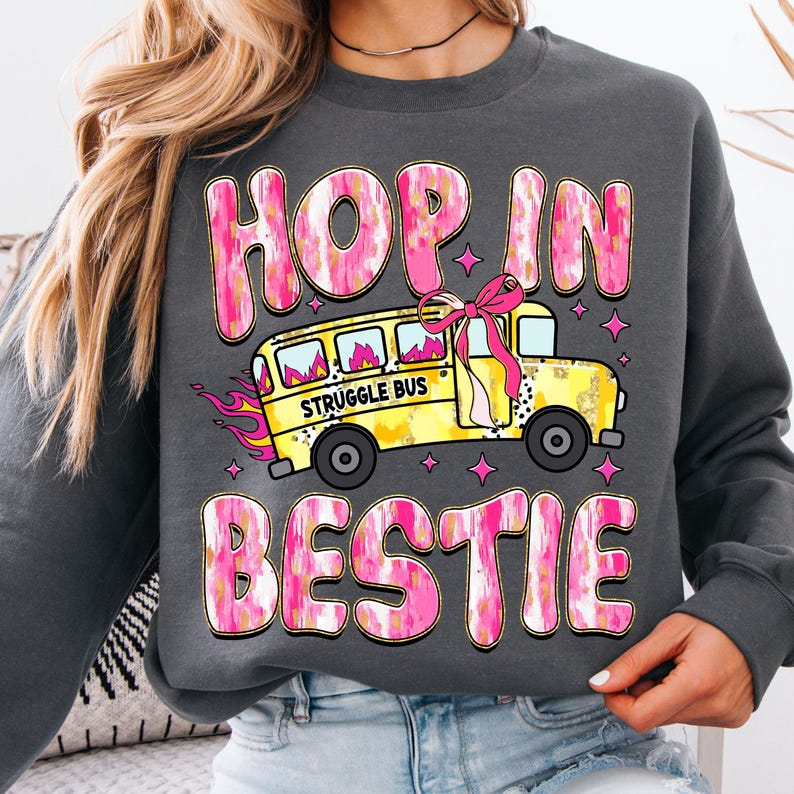 May include: A gray sweatshirt with a pink and gold graphic design that says "Hop in bestie" and features a yellow school bus with the words "Struggle Bus" on the side.