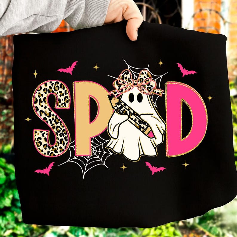 Pu&ograve; includere: T-shirt nero con la scritta "SPOD" in stampa leopardata, beige e rosa. Un fantasma con un fiocco leopardato e una matita al centro. Pipistrelli e stelle rosa circondano il testo e il fantasma.