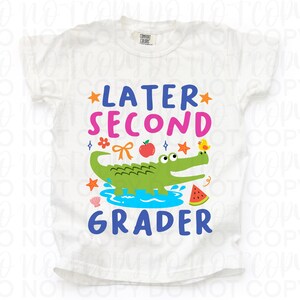 K&ouml;nnte beinhalten: Wei&szlig;es T-Shirt mit einem farbenfrohen Grafikdesign. Das Design zeigt den Text "LATER SECOND GRADER" mit Illustrationen eines Alligators, eines Vogels, eines Apfels und anderen Elementen zum Thema Schule. Das Shirt ist aus weichem Material.