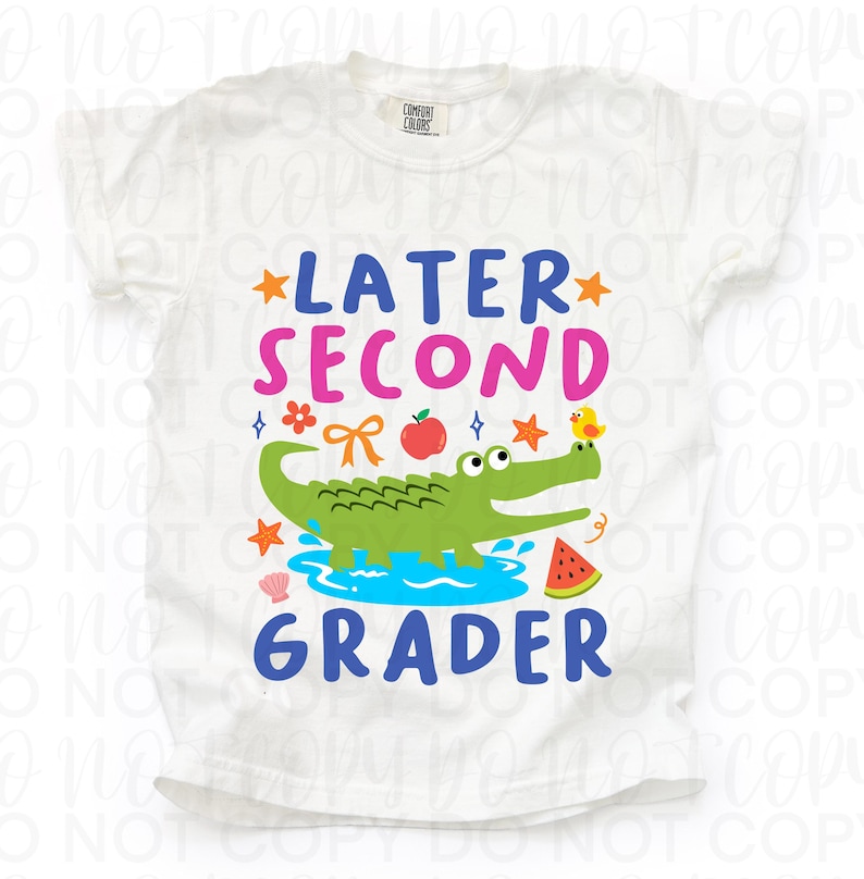 K&ouml;nnte beinhalten: Wei&szlig;es T-Shirt mit einem farbenfrohen Grafikdesign. Das Design zeigt den Text "LATER SECOND GRADER" mit Illustrationen eines Alligators, eines Vogels, eines Apfels und anderen Elementen zum Thema Schule. Das Shirt ist aus weichem Material.