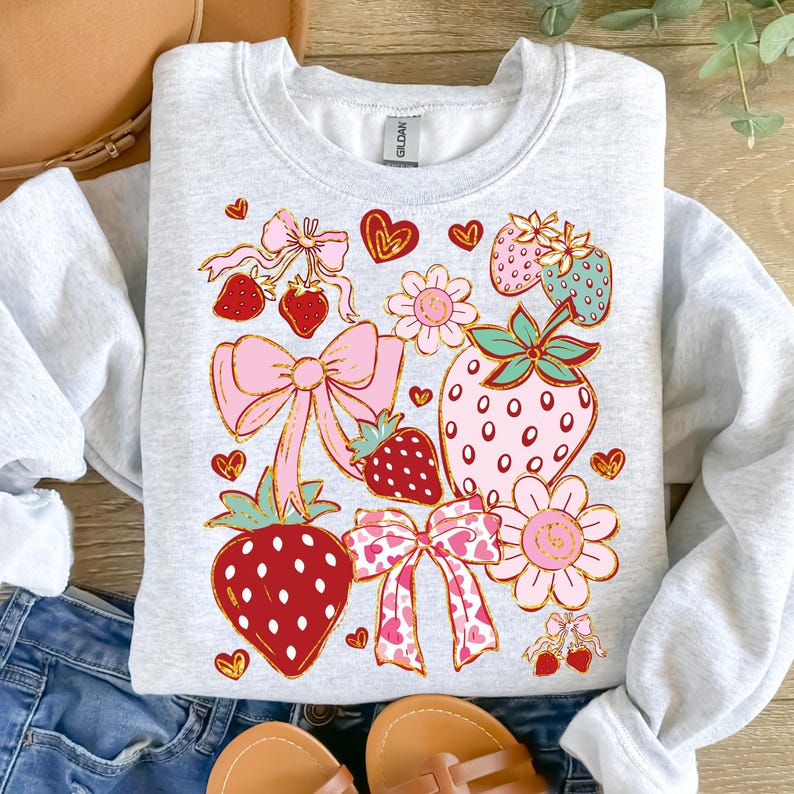 Op de afbeelding: Een grijs sweatshirt met een kleurrijk ontwerp van aardbeien, strikken en harten. Het ontwerp is in retro-stijl met een roze, rode en groene kleurstelling.