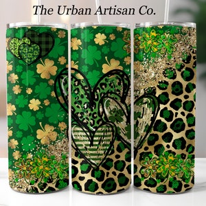 May include: Green and gold insulated tumbler with a St. Patrick's Day theme. The tumbler features shamrocks, leopard print hearts, and gold glitter accents. The text "The Urban Artisan Co." is at the top.