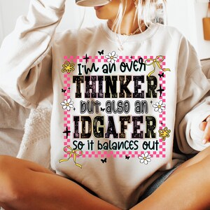 May include: A beige sweatshirt with the text "I'm an over THINKER but also an IDGAFER so it balances out." The text is in black, pink, and green, with floral and butterfly accents.