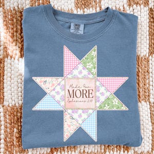 May include: A blue Comfort Colors crew neck t-shirt with a star-shaped patchwork design. The patchwork includes pink gingham, floral, and blue gingham patterns. The center of the star has the text "Made For MORE Ephesians 2:10".