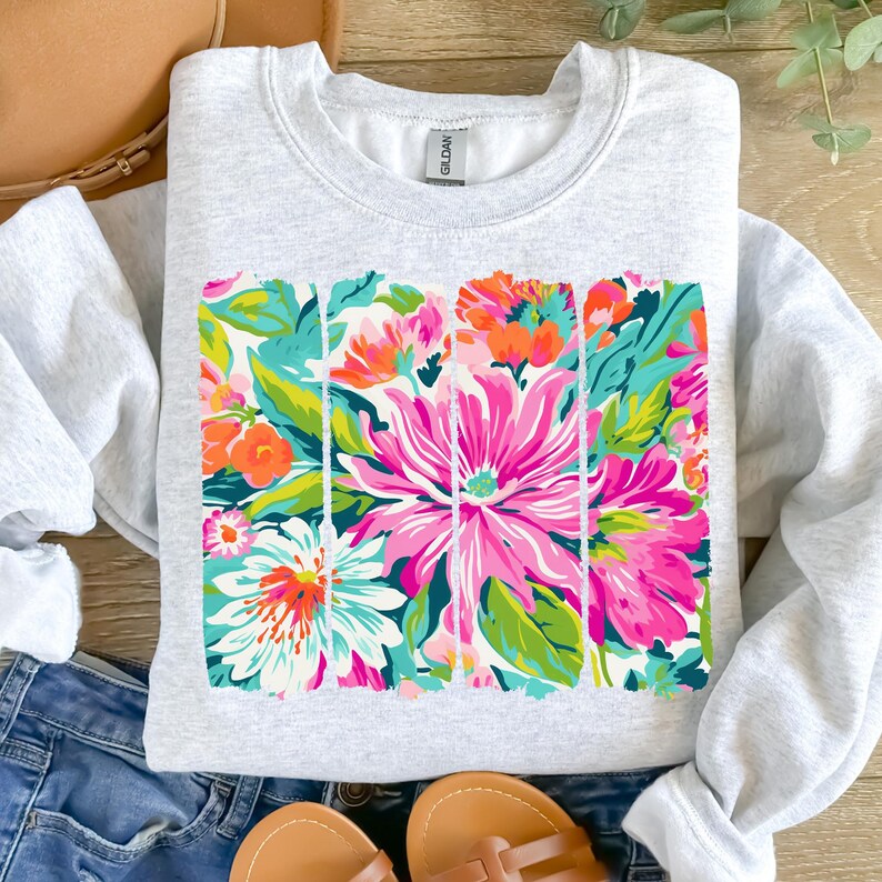 May include: A gray sweatshirt with a colorful floral print. The print features pink, orange, green, and blue flowers. The flowers are arranged in a vertical pattern with white outlines.