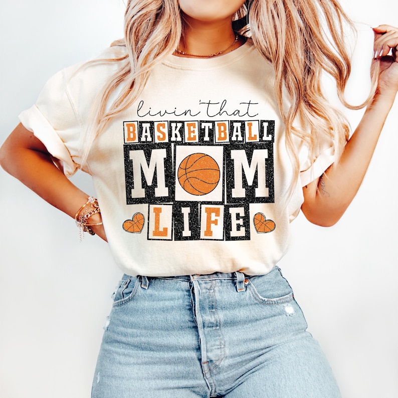 May include: A white t-shirt with the text "Livin' that Basketball Mom Life" in black and orange with a basketball graphic.
