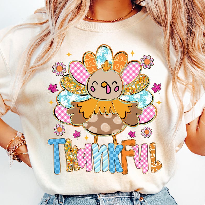 May include: A cream-colored sweatshirt featuring a cartoon turkey design with the word "Thankful" in colorful, patterned letters. The turkey has a brown body, orange feathers, and a cheerful expression, perfect for Thanksgiving.