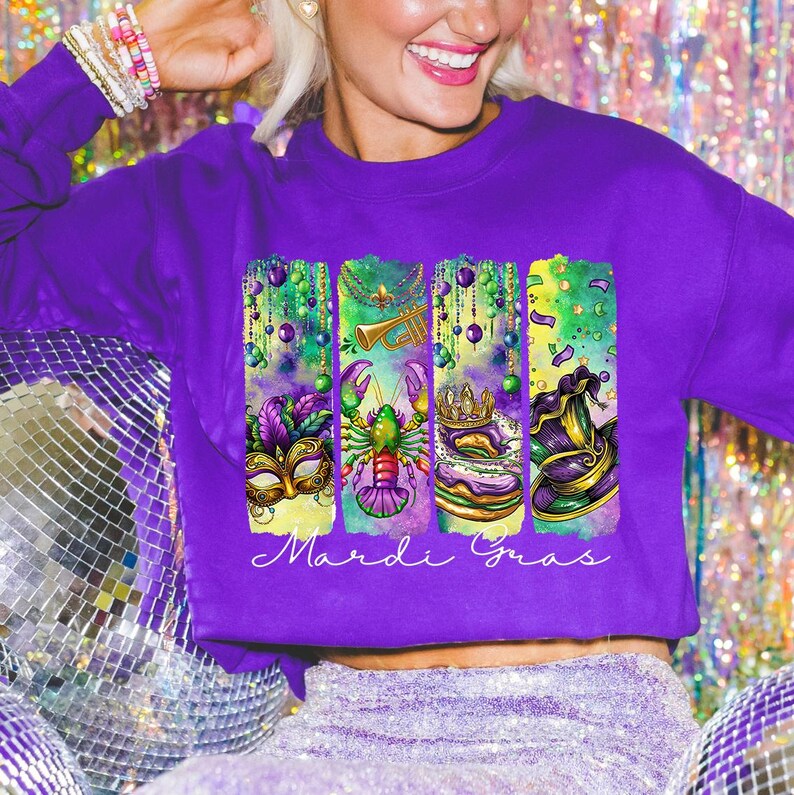May include: Purple sweatshirt with a graphic design of Mardi Gras themed elements, including a mask, a crawfish, a king cake, and a jester's hat. The text "Mardi Gras" is printed below the graphic.