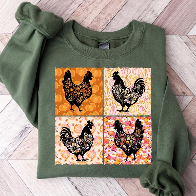 May include: An olive green sweatshirt featuring a four-panel design with black rooster silhouettes filled with floral patterns. The background panels include pumpkins and floral designs in orange, pink, and yellow. A fall-themed apparel item.