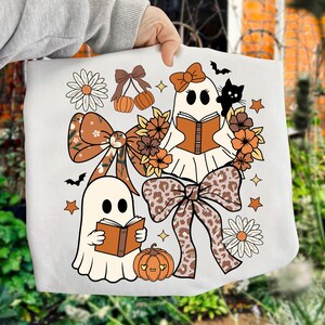 Op de afbeelding: Witte draagtas met een Halloween-ontwerp. Het ontwerp bevat twee spookfiguren die boeken lezen, omringd door pompoenen, strikken, bloemen, sterren en een zwarte kat. Het kleurenpalet omvat oranje, bruin en wit.