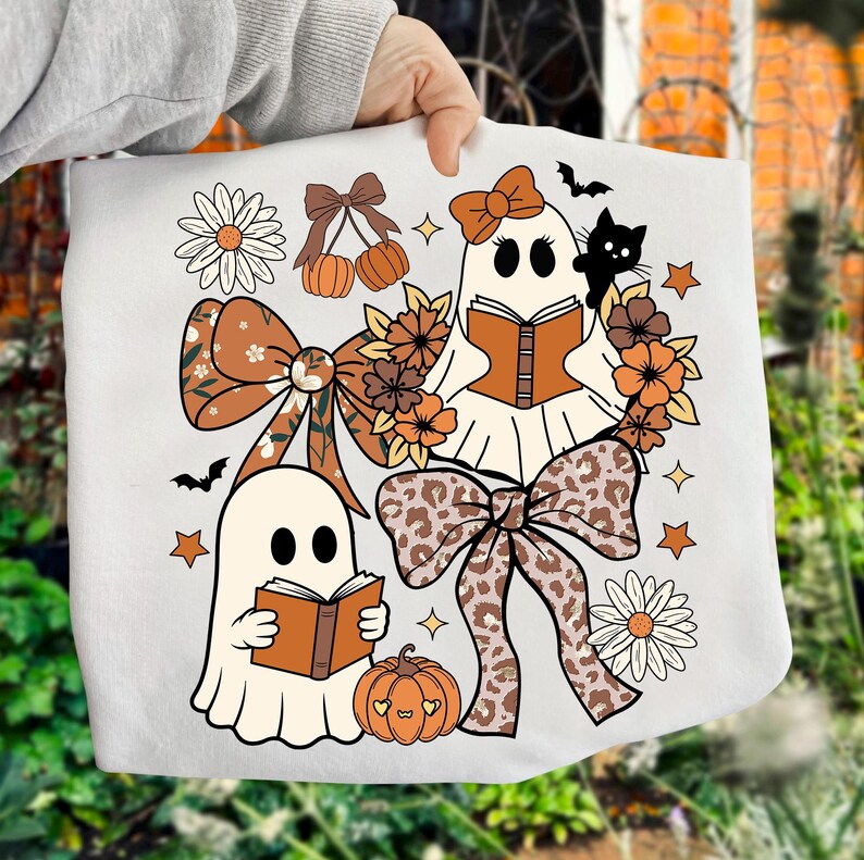 Op de afbeelding: Witte draagtas met een Halloween-ontwerp. Het ontwerp bevat twee spookfiguren die boeken lezen, omringd door pompoenen, strikken, bloemen, sterren en een zwarte kat. Het kleurenpalet omvat oranje, bruin en wit.