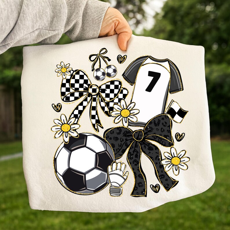 May include: A cream-colored soccer-themed design featuring a soccer ball, jersey with the number 7, bows, daisies, and a soccer glove. The design incorporates black, white, and gold accents, with a checkered pattern on some elements.