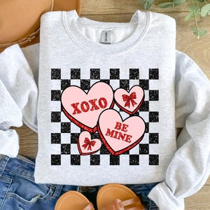 May include: A gray sweatshirt with a checkered pattern and pink heart-shaped candy with the words "XOXO" and "BE MINE" on them.