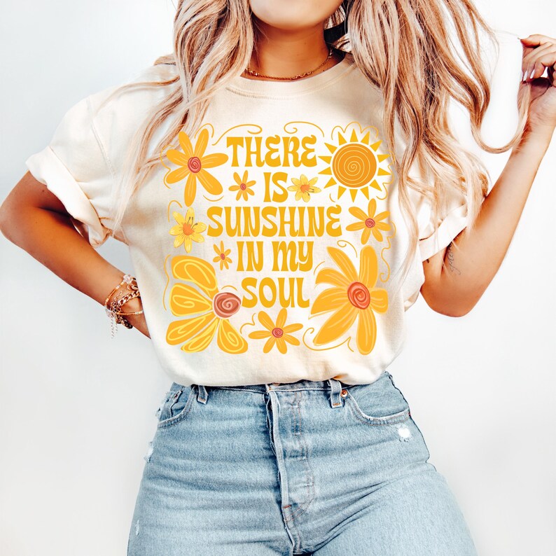 May include: A white t-shirt with a yellow and orange graphic design featuring flowers and a sun. The text on the shirt reads "There is sunshine in my soul."