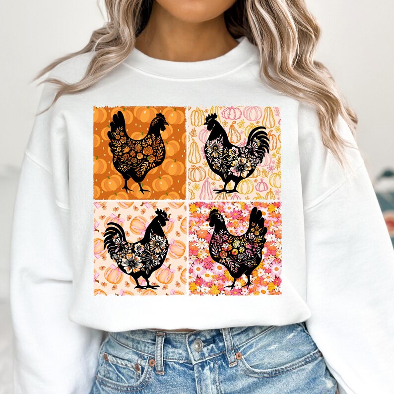 May include: White sweatshirt featuring a four-panel design with black rooster silhouettes filled with floral patterns. The background panels showcase pumpkins in orange and pink hues, creating a fall-themed aesthetic.