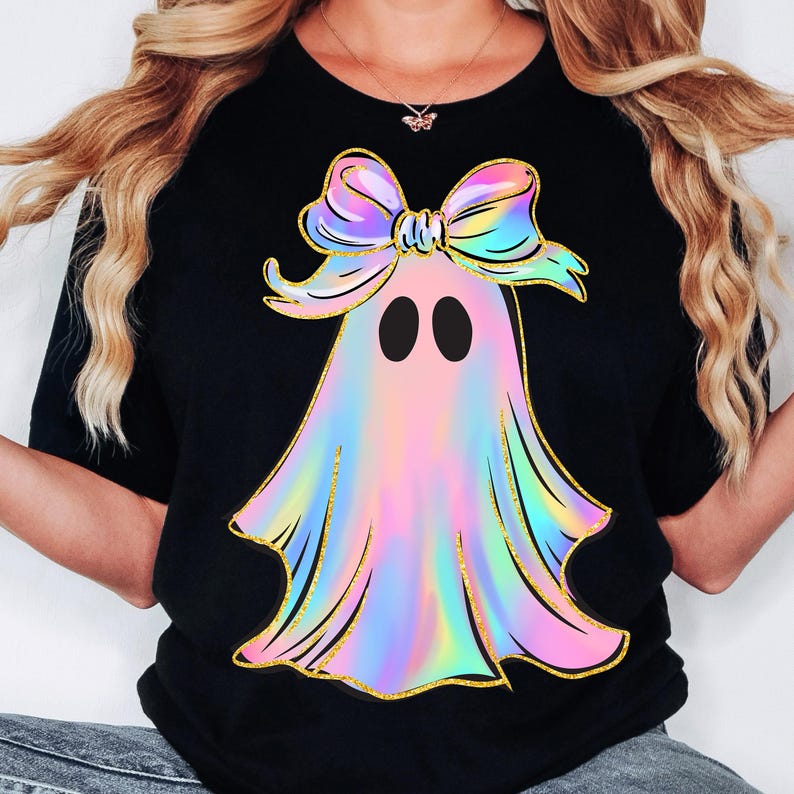 May include: Black t-shirt featuring a colorful ghost design. The ghost has a pastel rainbow body, black eyes, and a large bow. The design is outlined in gold glitter.