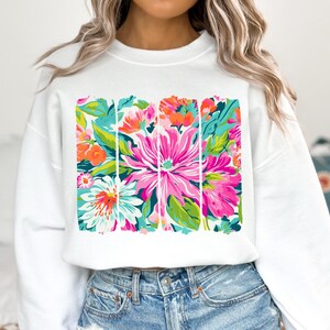 May include: White sweatshirt with a colorful floral print design. The print features a variety of flowers in shades of pink, orange, white, and green.