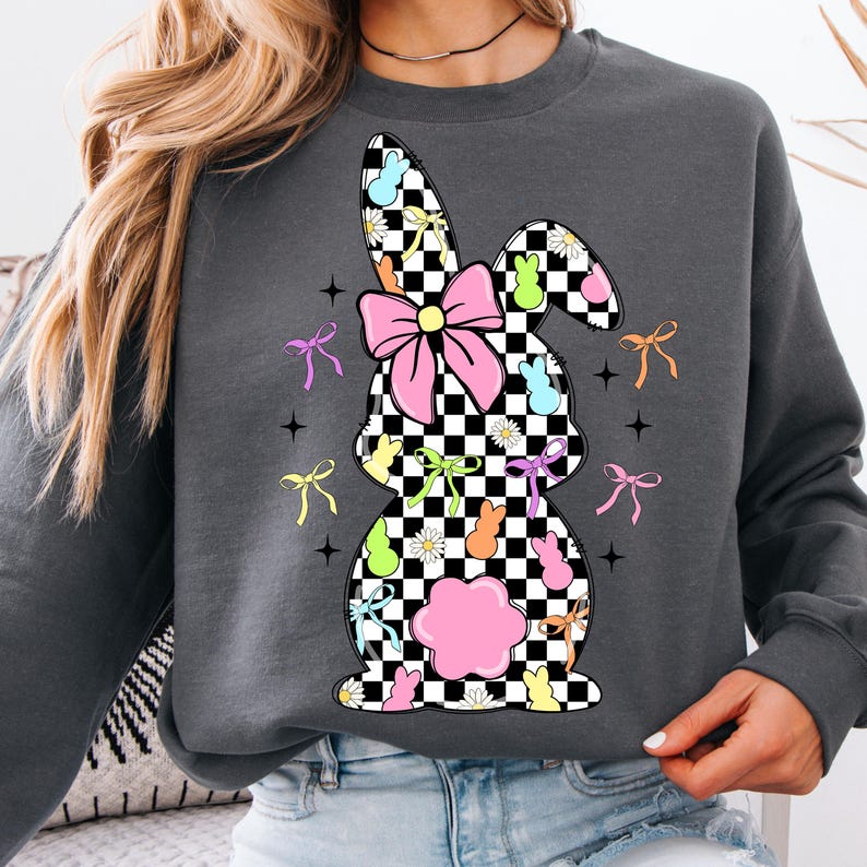 May include: A gray sweatshirt with a checkered bunny silhouette. The bunny is decorated with pastel-colored jelly beans, bows, and flowers.