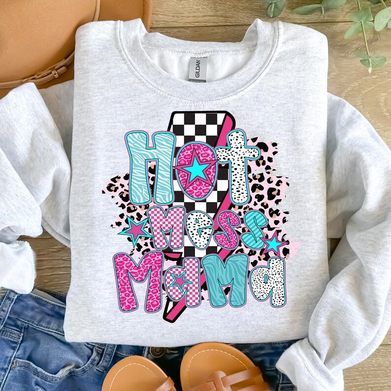 May include: A gray sweatshirt with the text "Hot Mess Mama" in pink, blue, and black letters. The letters are surrounded by a checkered pattern, animal print, and stars.