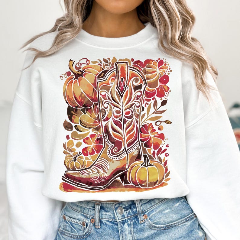 Op de afbeelding: Witte sweatshirt met een aquarelontwerp van een cowboylaars, pompoenen en herfstbladeren in oranje, bruin en rood. De laars heeft ingewikkelde details. Het ontwerp heeft een herfstthema.