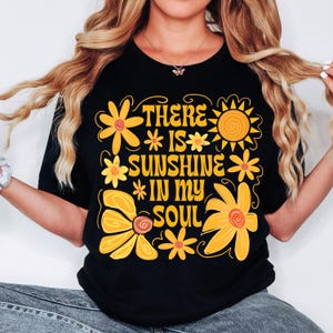 May include: Black t-shirt with a yellow and orange floral design and the text "There is sunshine in my soul".