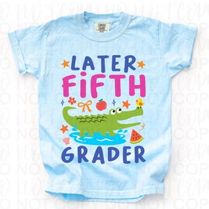 K&ouml;nnte beinhalten: Hellblaues T-Shirt mit dem Schriftzug "LATER FIFTH GRADER" in Pink und Blau. Ein gr&uuml;nes Alligatoren-Motiv, ein roter Apfel, ein gelbes K&uuml;ken und eine Wassermelone sind ebenfalls abgebildet.