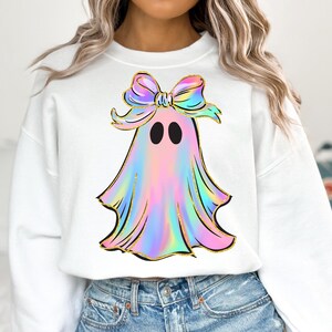May include: White sweatshirt featuring a colorful ghost design with a bow. The ghost has a pastel rainbow color scheme with gold accents. The bow is also rainbow-colored. The design is centered on the front of the sweatshirt.