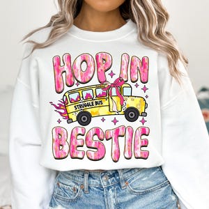May include: White sweatshirt with a pink and gold graphic design that says "Hop in bestie" with a yellow school bus that says "Struggle Bus" on the side.