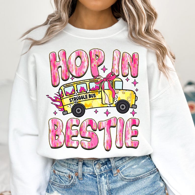 May include: White sweatshirt with a pink and gold graphic design that says "Hop in bestie" with a yellow school bus that says "Struggle Bus" on the side.