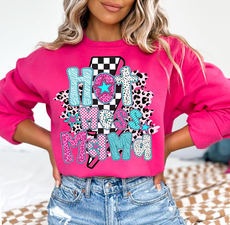 May include: Pink sweatshirt with a graphic print of a lightning bolt with a checkered pattern and the text "Hot Mess Mama" in pink, blue, and black with animal print accents.