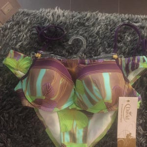 May include: A two-piece bikini set featuring a purple, light blue, and lime green tropical leaf pattern. The top has molded cups with purple straps and gold-tone hardware. A beige product tag with the text David Il Costume da Bagno is attached.