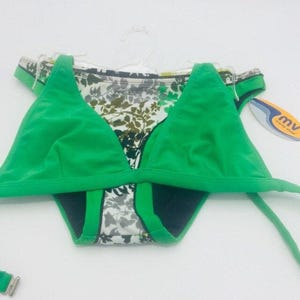 Pode incluir: Um conjunto de biquíni verde brilhante composto por um top e uma parte de baixo a condizer com uma estampa botânica de folhas em branco, preto e verde-azeitona. O fato de banho inclui alças finas, copas triangulares e uma etiqueta mv merés vivas.