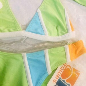 May include: A two-piece bikini set featuring a color-blocked design in lime green, sky blue, and orange with white trim accents. The bikini includes a triangle top and matching bottoms, with a tag attached that reads samba mar beachwear.