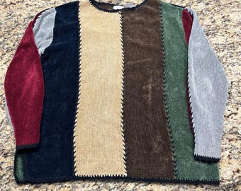May include: A long-sleeve pullover sweater featuring a vertical color-blocked design in shades of burgundy, navy blue, tan, brown, and forest green. The panels are joined by visible black whipstitch detailing along the seams, with a round neckline.