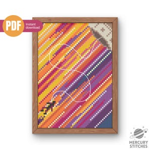 Op de afbeelding: Een ingelijst kruissteekpatroon met een diagonaal verloop van oranje, roze en paarse vierkantjes. Een dunne witte lijn loopt in een bocht door het midden en verbindt met een klein zwart figuurtje linksonder. Het ontwerp bevat een hoekdetail.