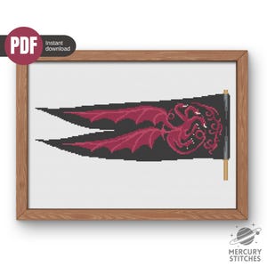 Peut inclure: Un modèle de point de croix représentant un drapeau noir à deux pointes orné d'un dragon à trois têtes dans des tons rouge foncé. Le dragon est représenté avec les ailes déployées et les queues enroulées. Le motif est dans un cadre en bois.